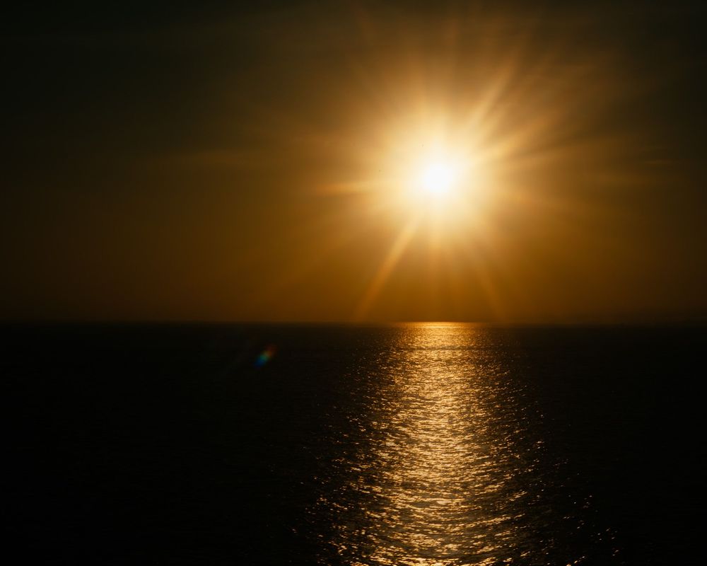 Golden sun setting over dark ocean waters creating a dramatic glow.