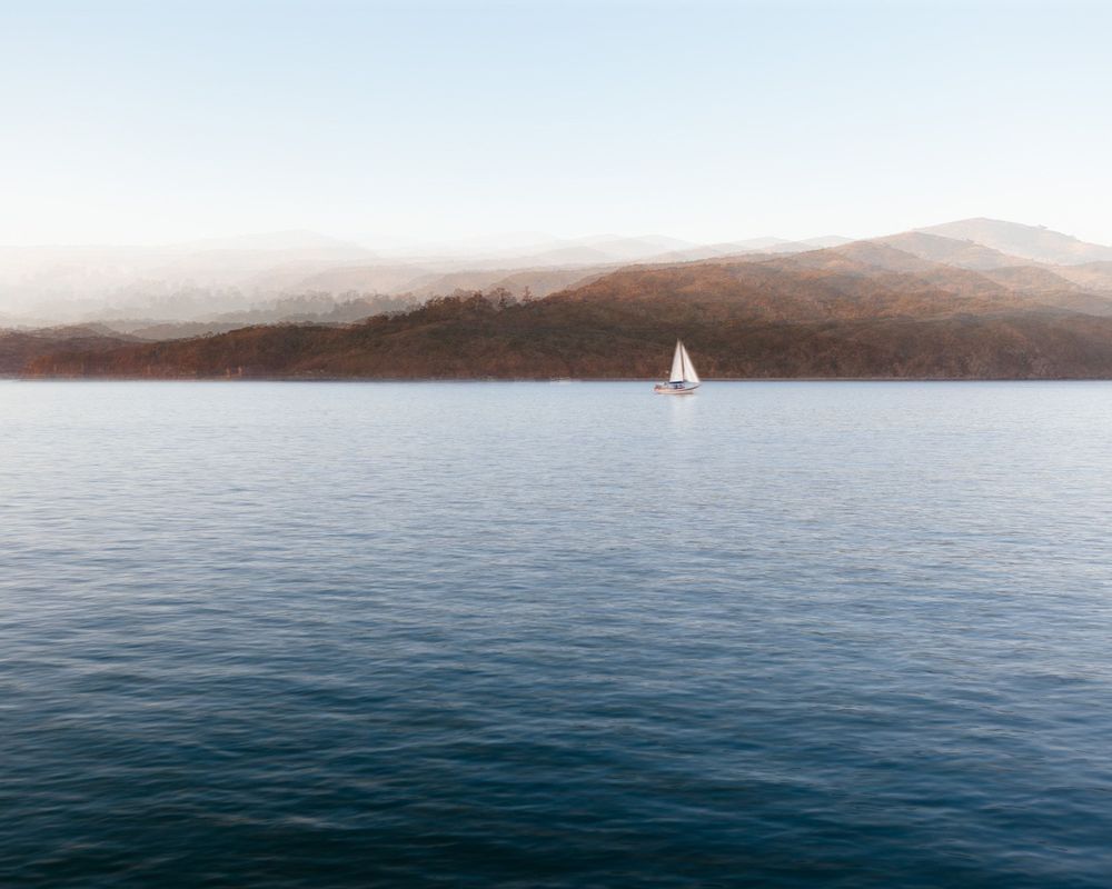 Serene seascape with distant hills and a lone sailboat on calm waters.