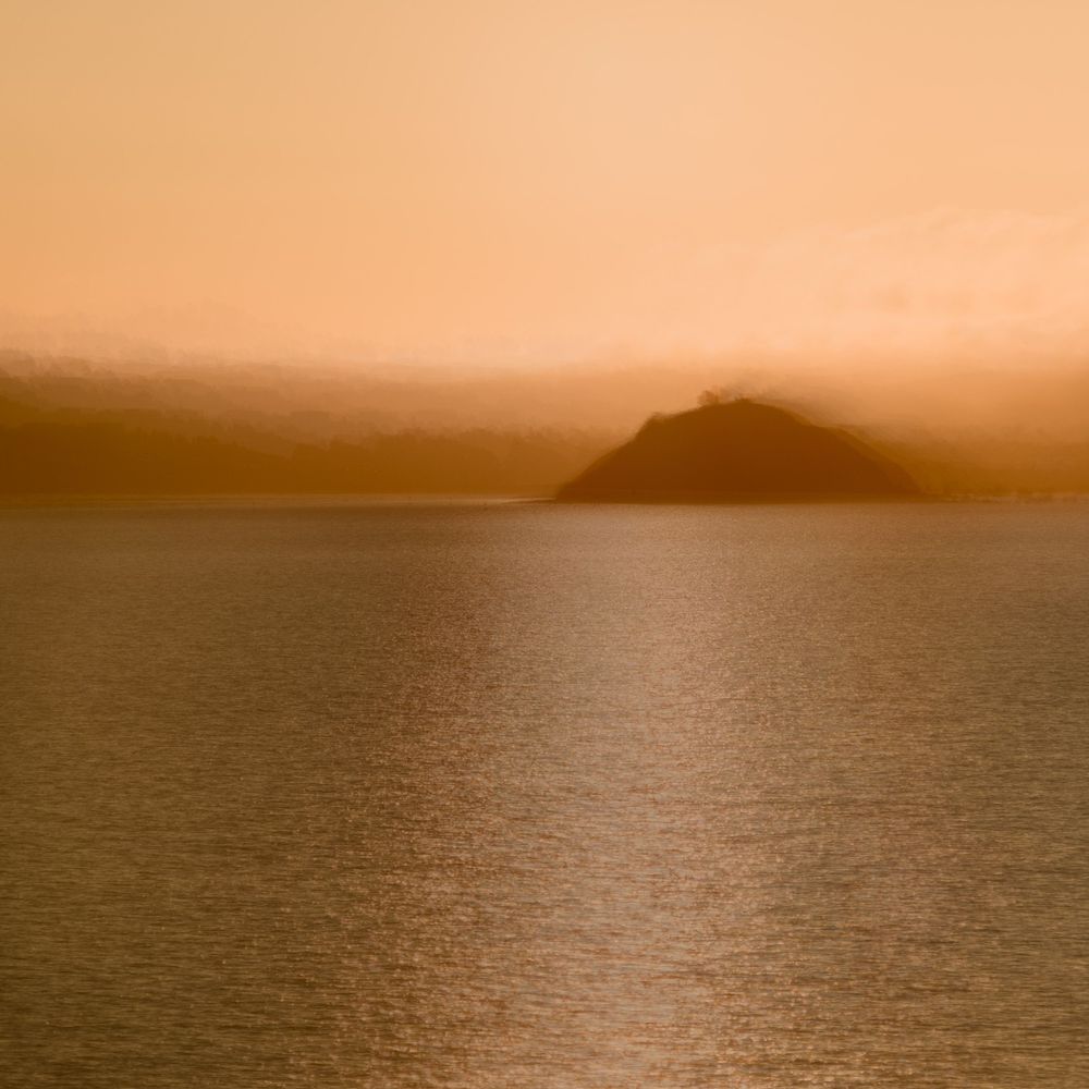 Tranquil ocean horizon at sunset with warm orange glow reflecting off calm waters.