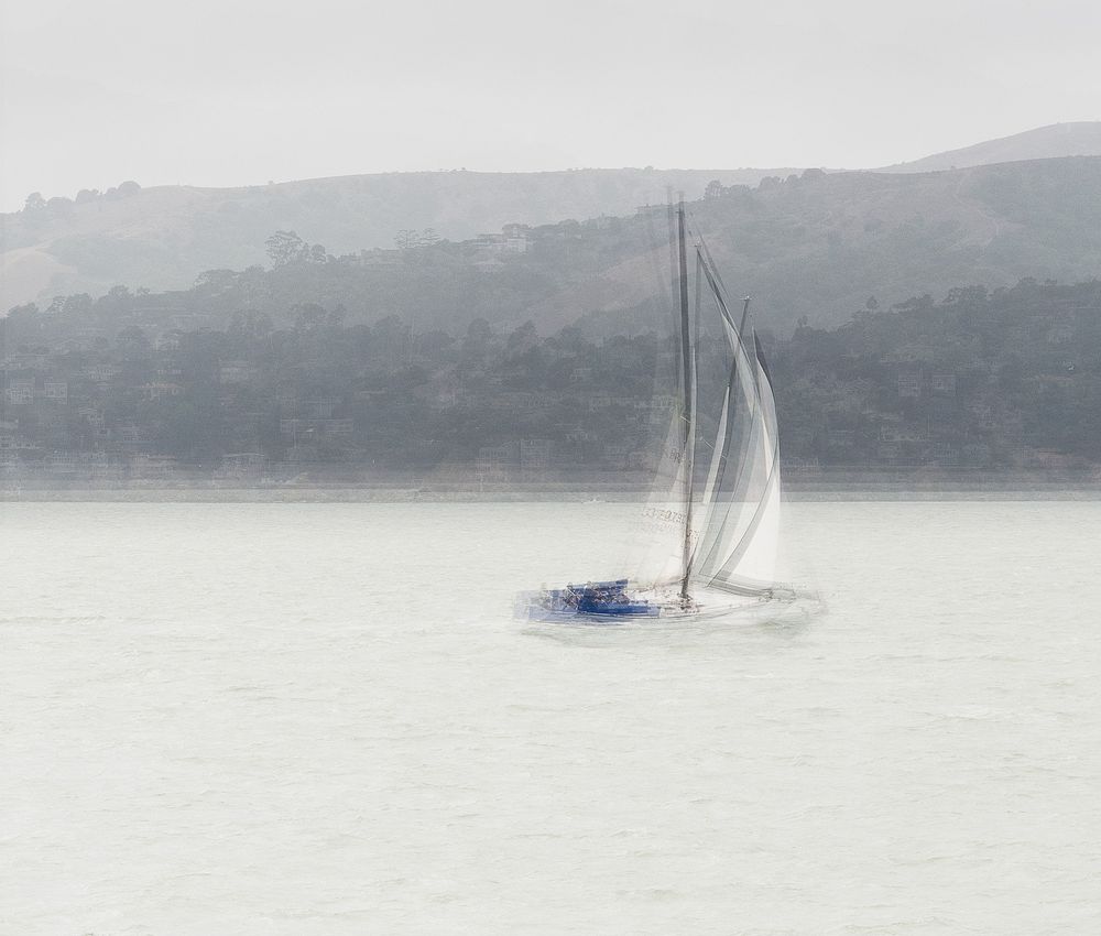 Sailboats gliding across misty waters with rolling hills in the background.