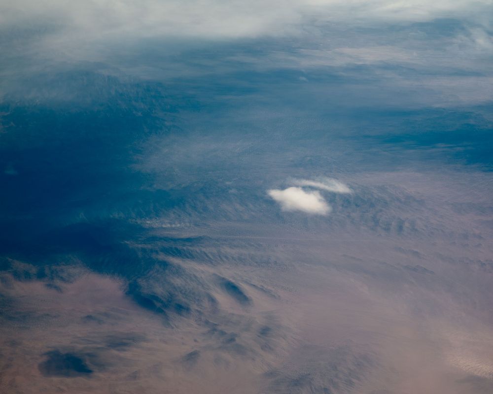 Aerial view of desert landscape with mountains and scattered clouds.