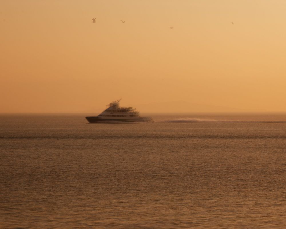 Silhouette of a yacht cruising on calm waters during a golden sunset.