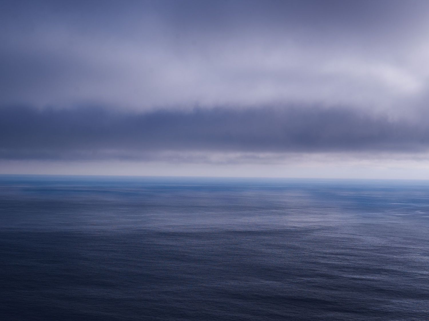 A panoramic seascape with moody cloudy skies over a calm ocean stretching to the horizon.