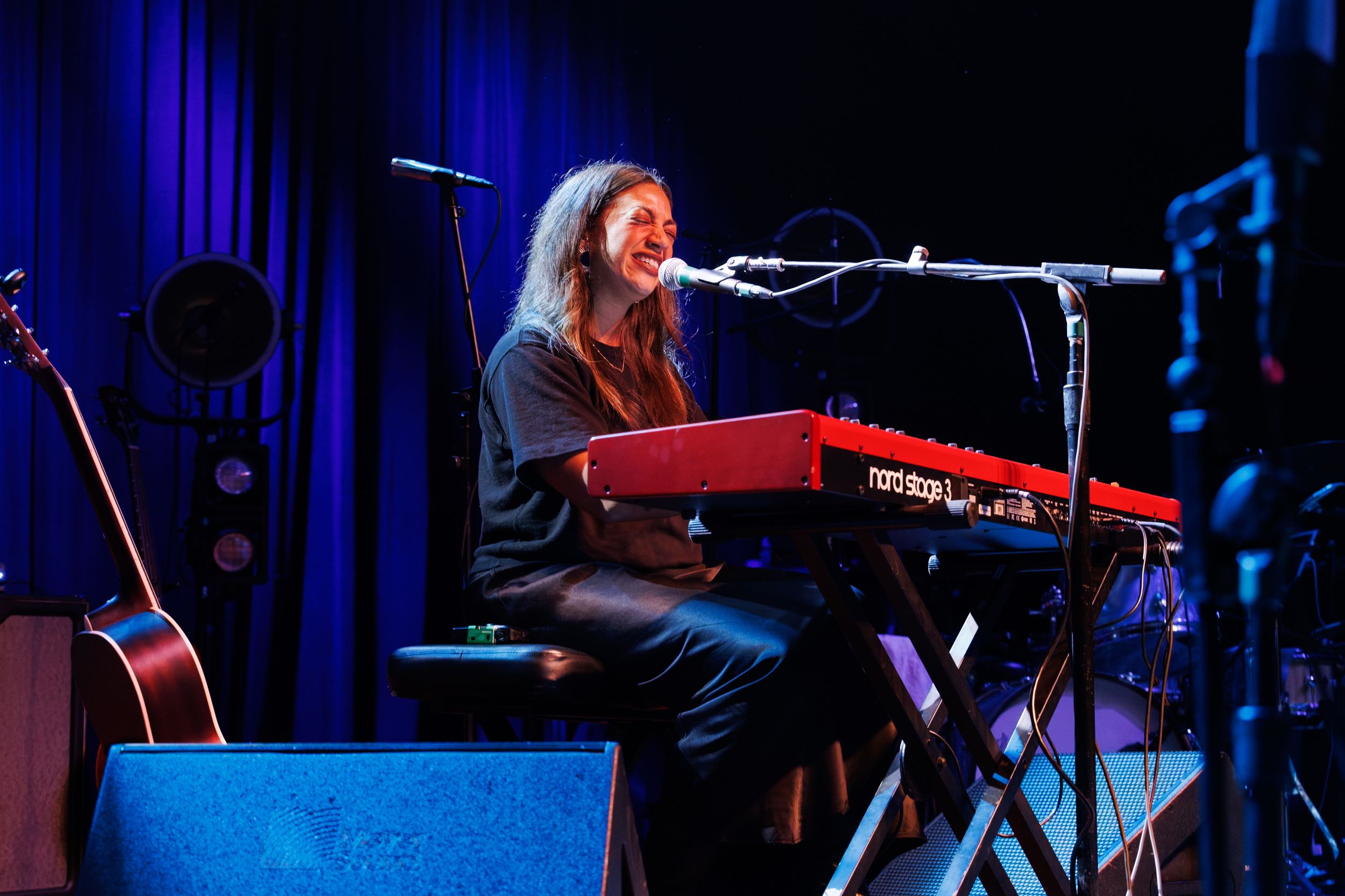 Concert performer illuminated by blue stage lights plays keyboard during a live music performance.