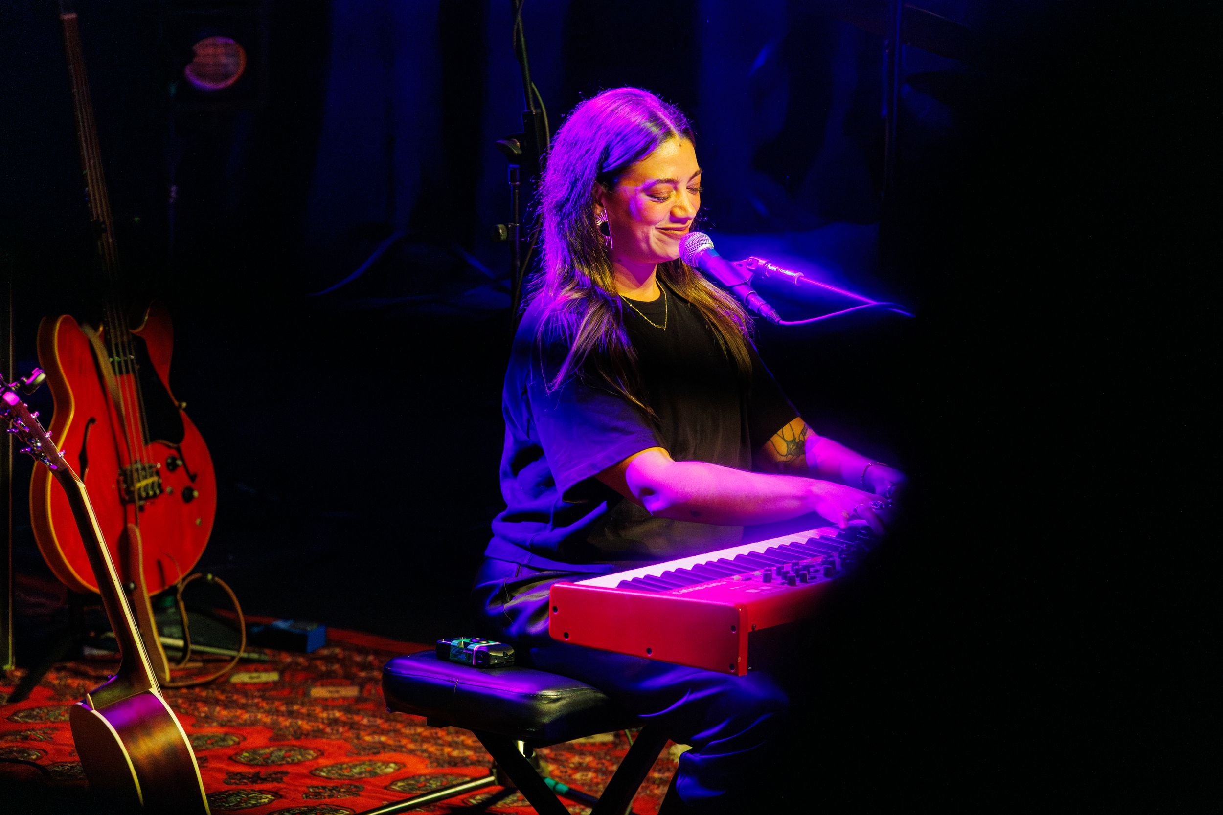 Musician performs on stage with dramatic purple and blue lighting creating an atmospheric mood.