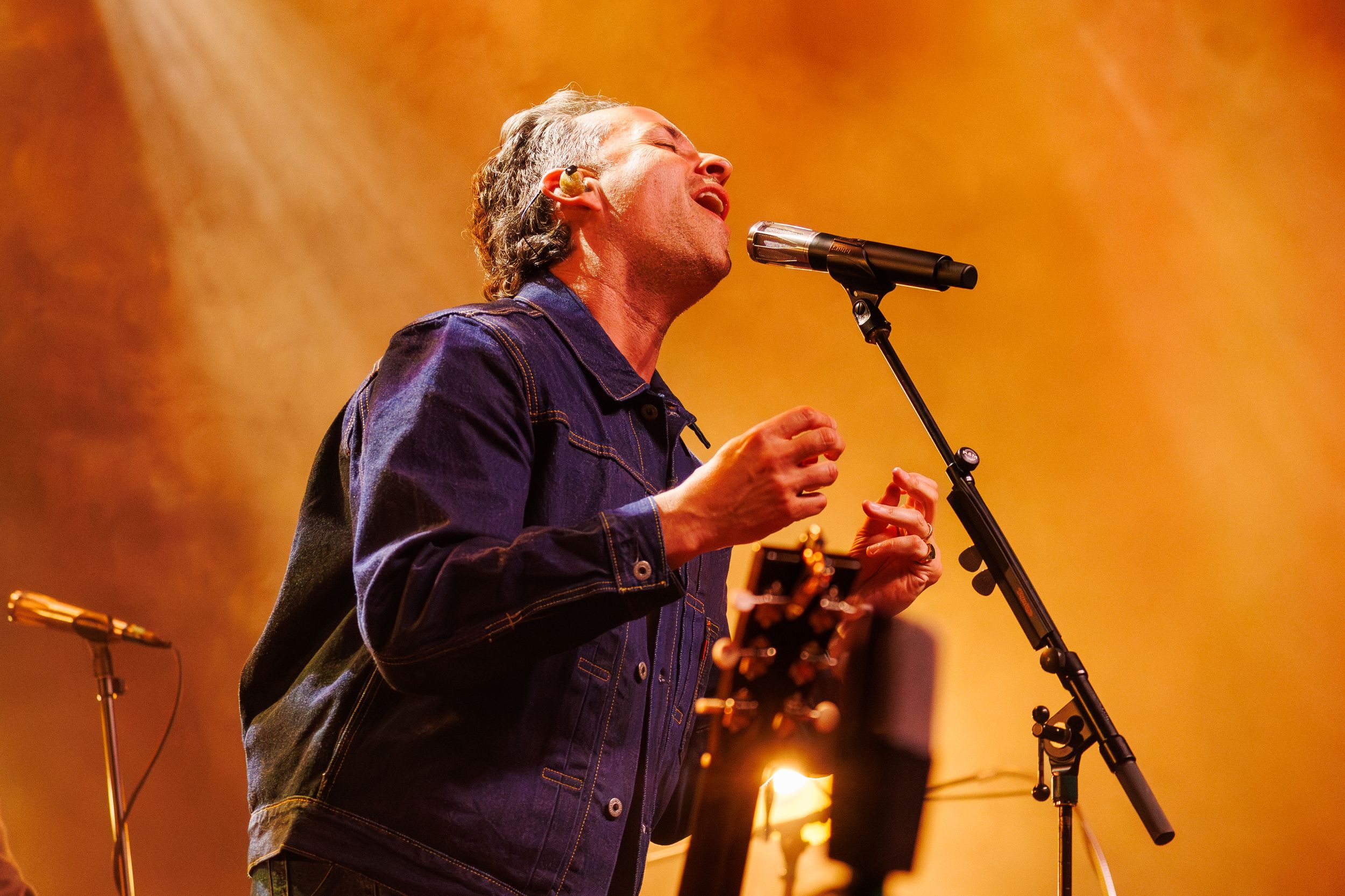 A performer sings passionately on stage with dramatic orange lighting creating a vibrant concert atmosphere.