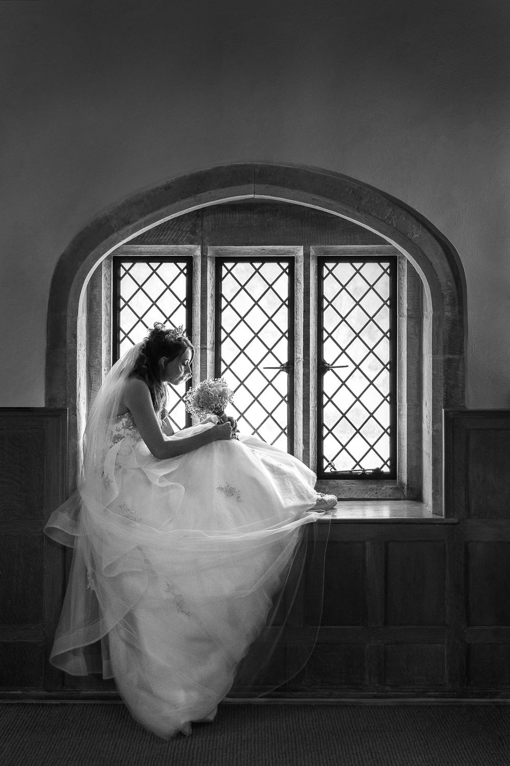 Black and white shot of bride sitting in medieval window at Michelham Priory, East Sussex