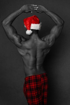 Charleston men’s fitness studio portrait of muscular man wearing Santa hat against dark background.