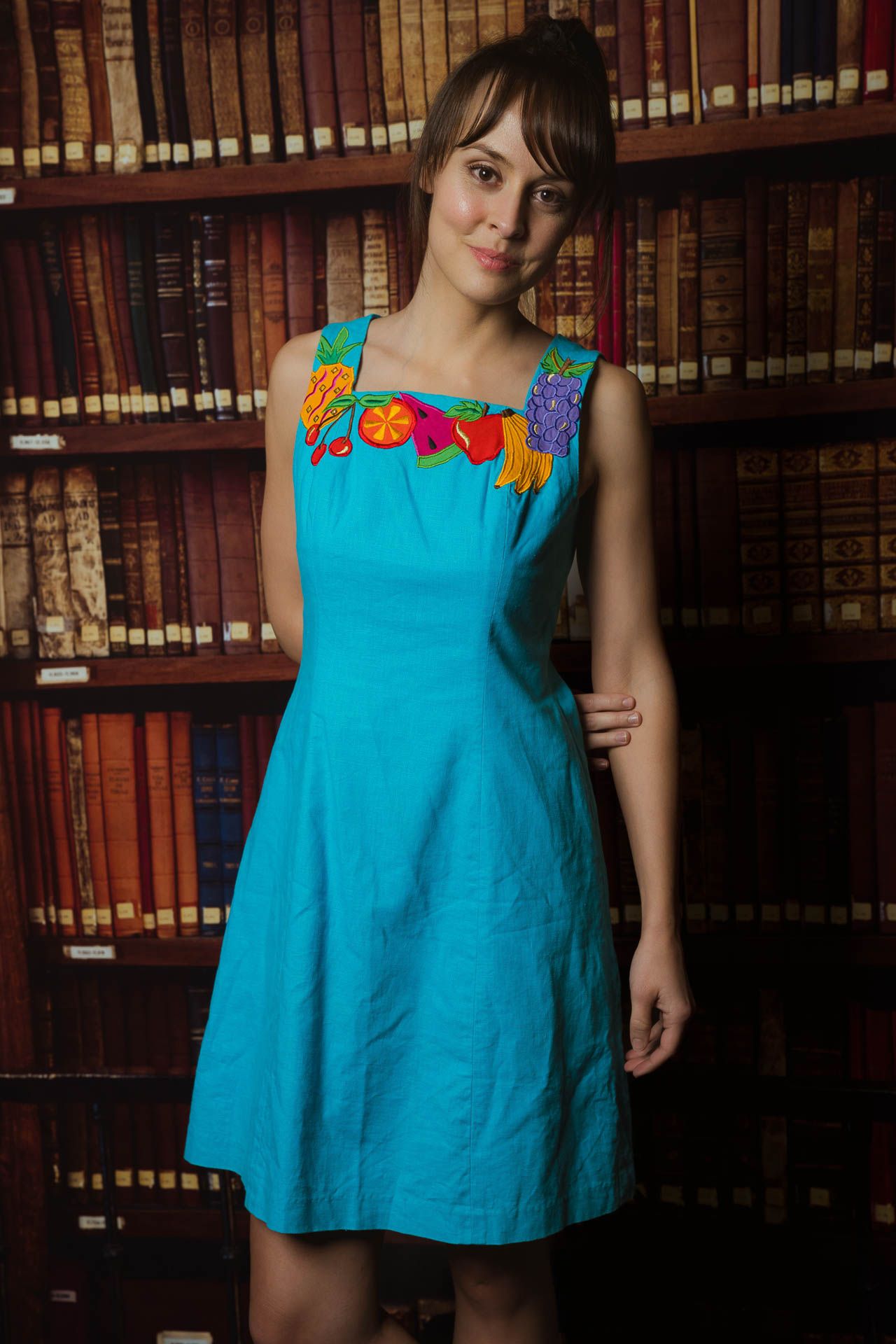 Charleston studio portrait of woman in turquoise dress against vintage library bookshelf backdrop.