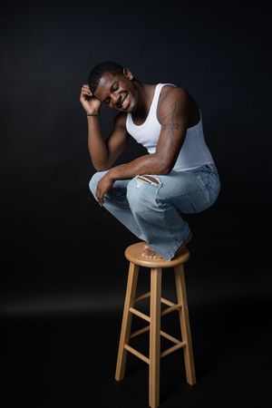 Charleston lifestyle studio portrait of male model smiling while seated on stool with dark background
