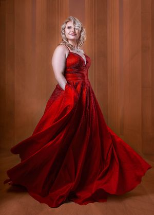 A flowing red velvet gown twirls elegantly against a warm brown studio backdrop in Charleston, SC