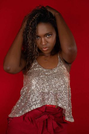 Charleston glamour studio portrait of woman in gold sequin top on red background.