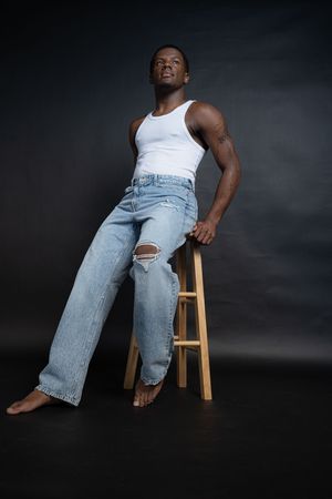 Charleston men’s studio portrait of confident male model seated on stool against dark backdrop