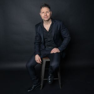Professional Charleston men’s studio portrait of man seated on stool against dark background.