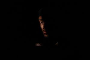 Low-key portrait in studio showing half a face emerging from darkness with subtle lighting in Charleston, SC