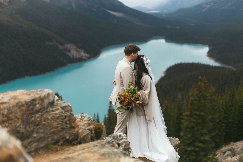 groom kisses bride's hair as she gazes out over a mountain lake in Banff National Park during their elopement