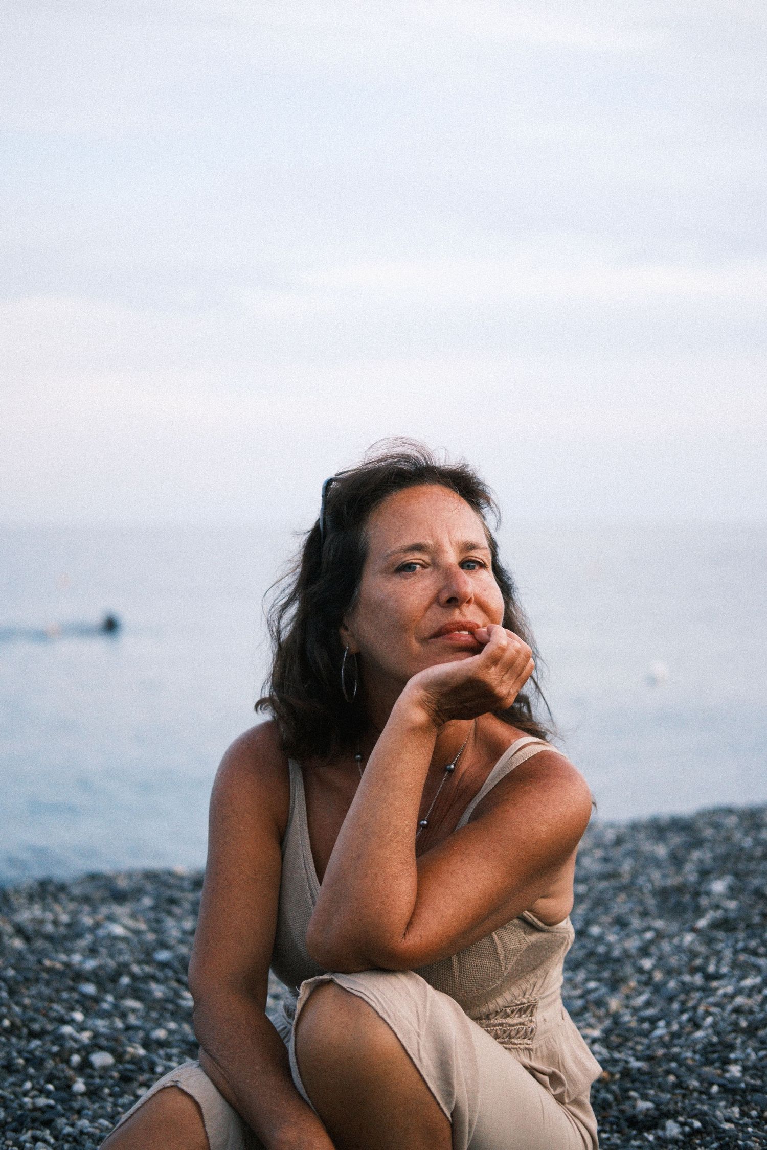A person lies on a rocky beach looking thoughtfully toward the horizon at sunset.