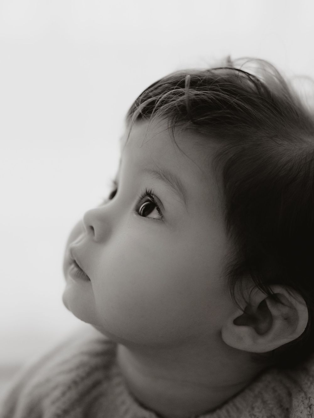 Black and white artistic portrait series showing a child's profile view looking upward against a white background.
