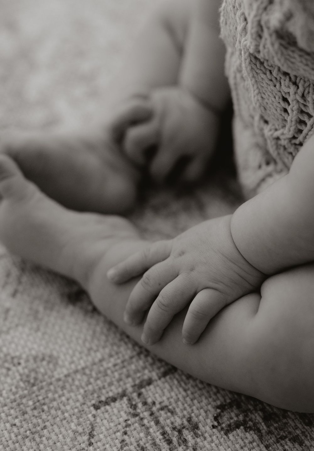 Close-up black and white photograph of a tiny baby hand resting on textured fabric.