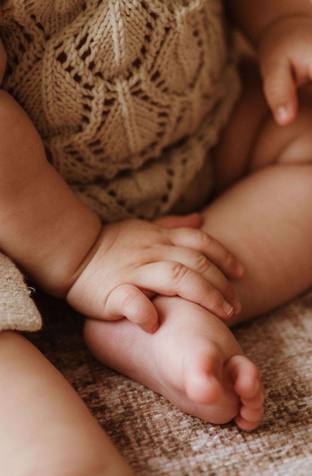 Close-up of tiny baby feet wrapped in a cozy brown knit blanket showing delicate toes and soft skin.