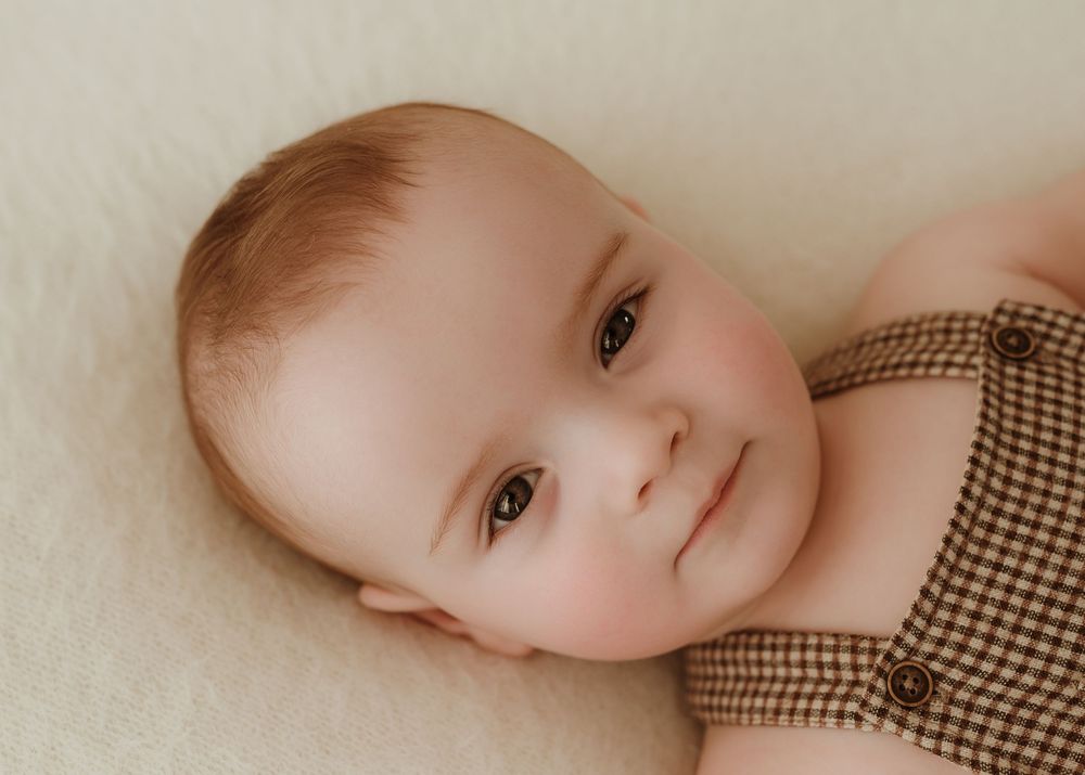 A series of seven connected photos showing a baby in a brown checkered outfit lying on a cream colored background.
