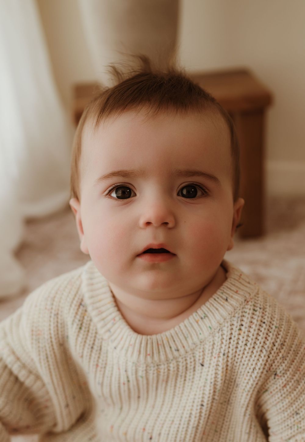 A sweet baby wearing a cozy cream knit sweater poses for a close-up portrait.