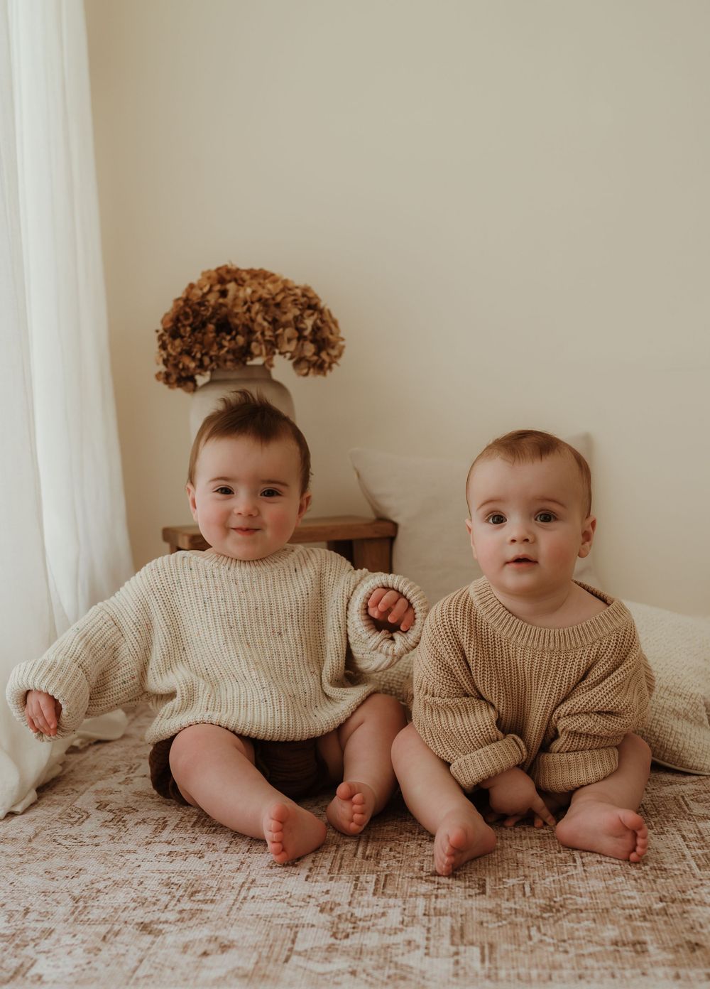 Four babies in matching cream sweaters sit together on a textured blanket.