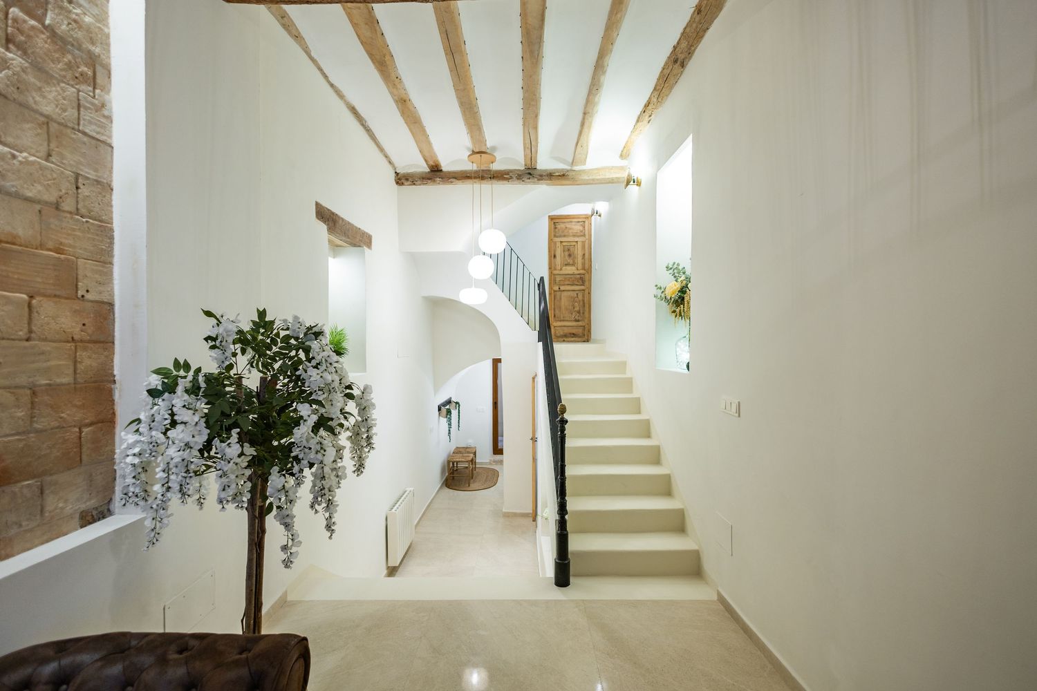 Modern white interior hallway with exposed wooden beams and brick walls featuring minimalist architectural design.