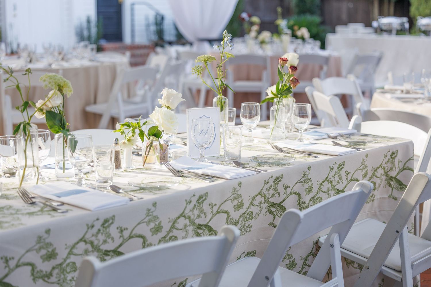 Elegant white wedding reception tables decorated with floral centerpieces and place settings in an outdoor setting.