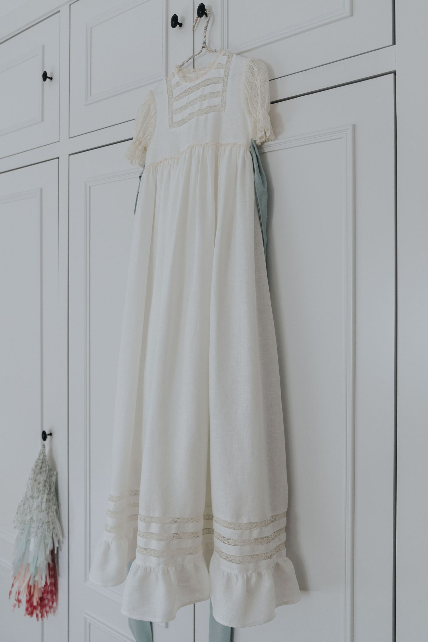 White vintage-style dresses and garments hanging on white wooden closet doors in a minimalist setting.