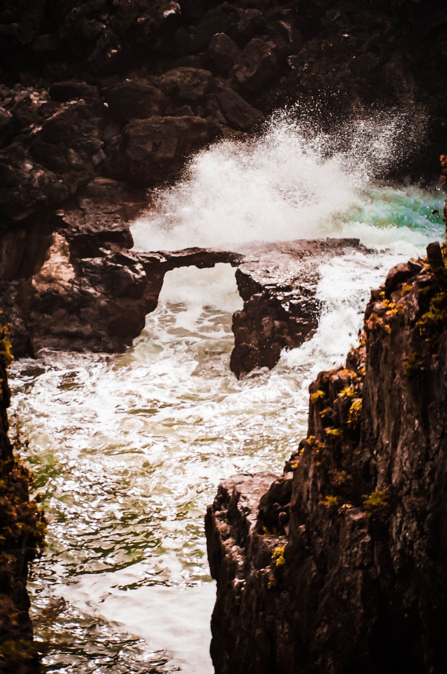 Dramatic sequence of ocean waves crashing against dark rocky cliffs with white foam spraying in the air.