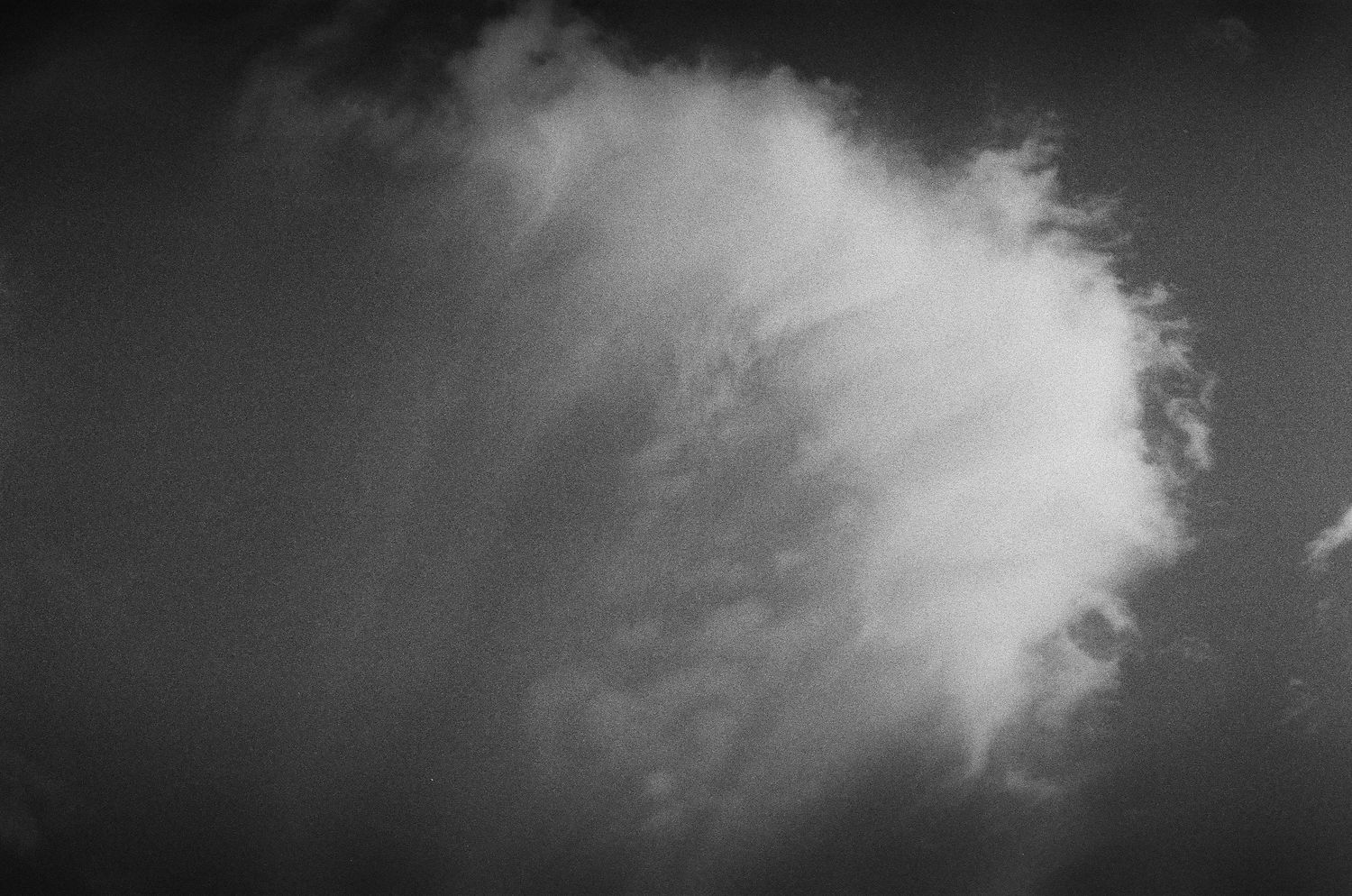 Dramatic black and white photograph of a billowing white cloud formation against a dark sky.