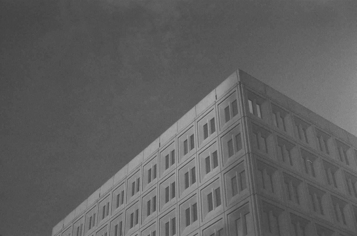 Black and white architectural photograph showing a modern building with repeating window patterns and geometric lines.