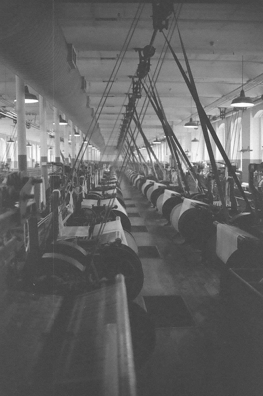 Vintage black and white photograph of an industrial textile factory floor with rows of spinning machinery.