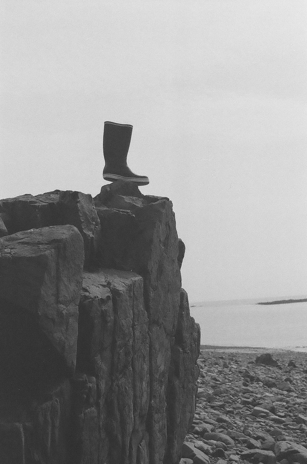 Black and white photograph of rugged coastal cliffs with geometric rock formations against an overcast sky.