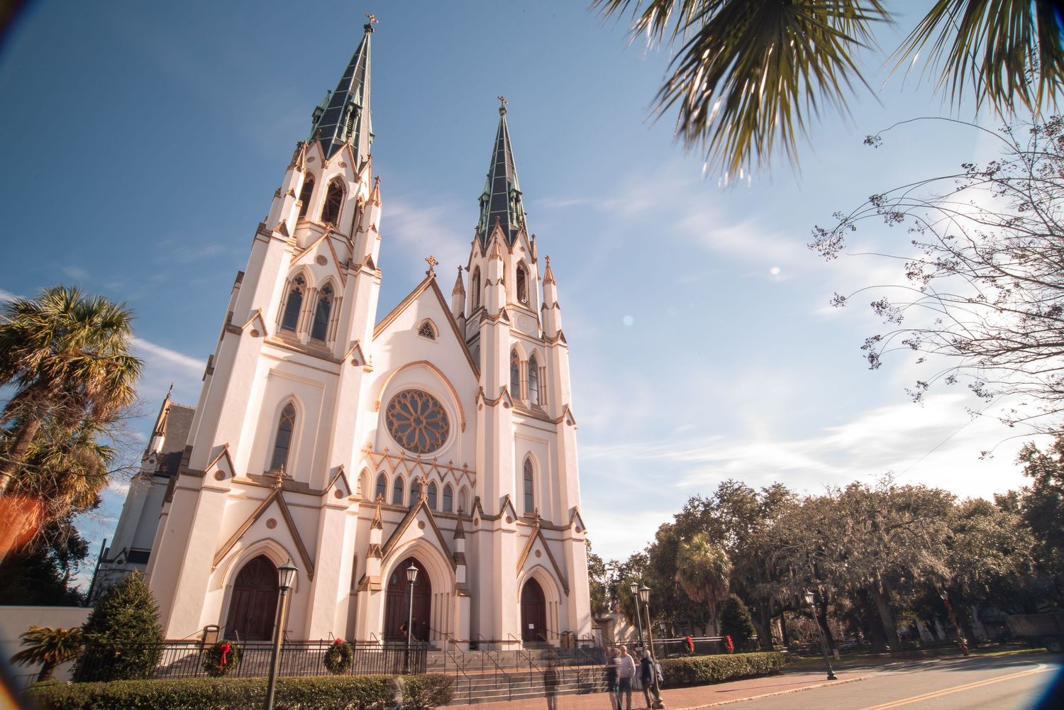 Historic white Gothic cathedral with twin spires and palm trees in Savannah Georgia on a sunny day.