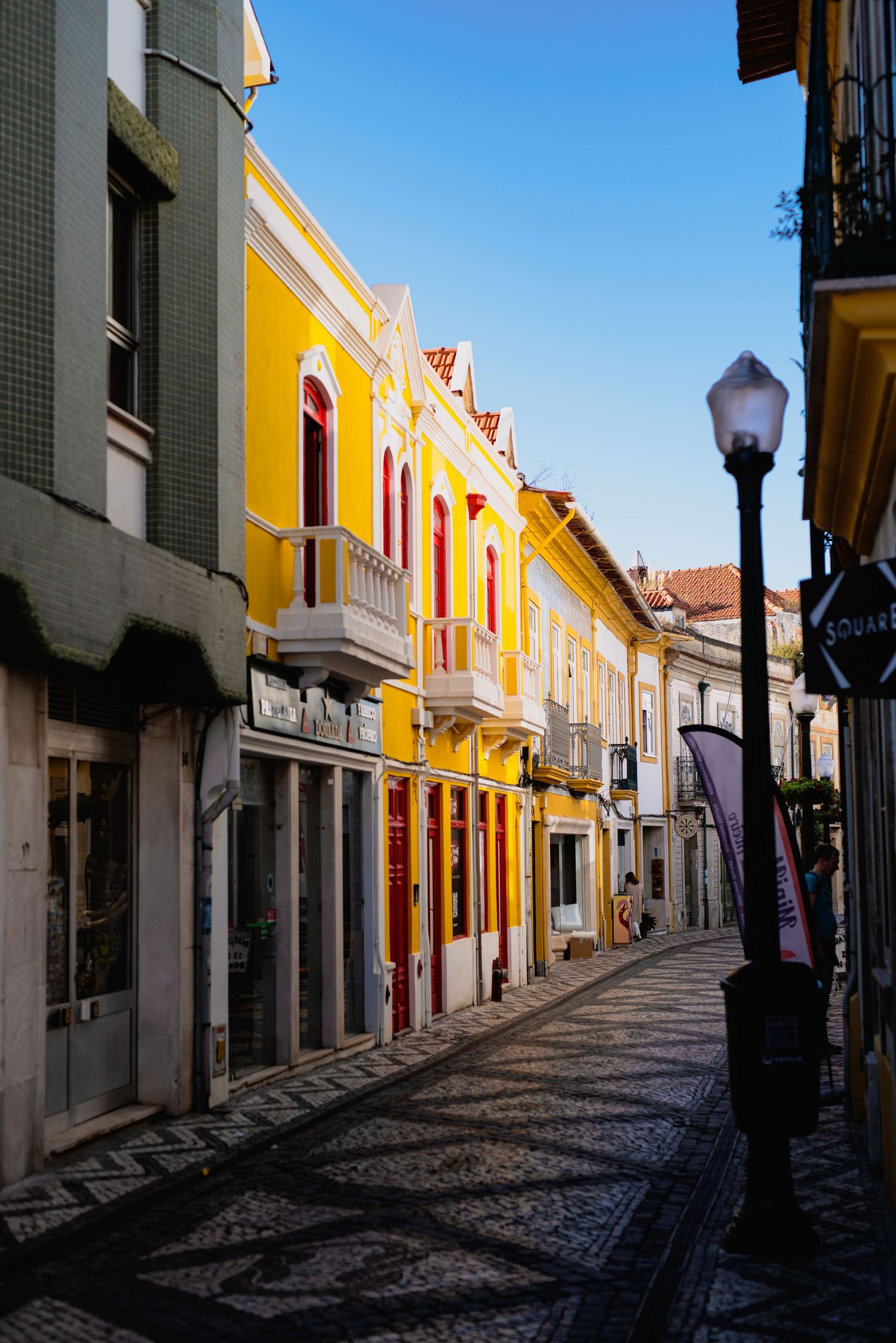 Colorful colonial buildings with yellow facades line a historic cobblestone street with vintage lamp posts in Portugal.