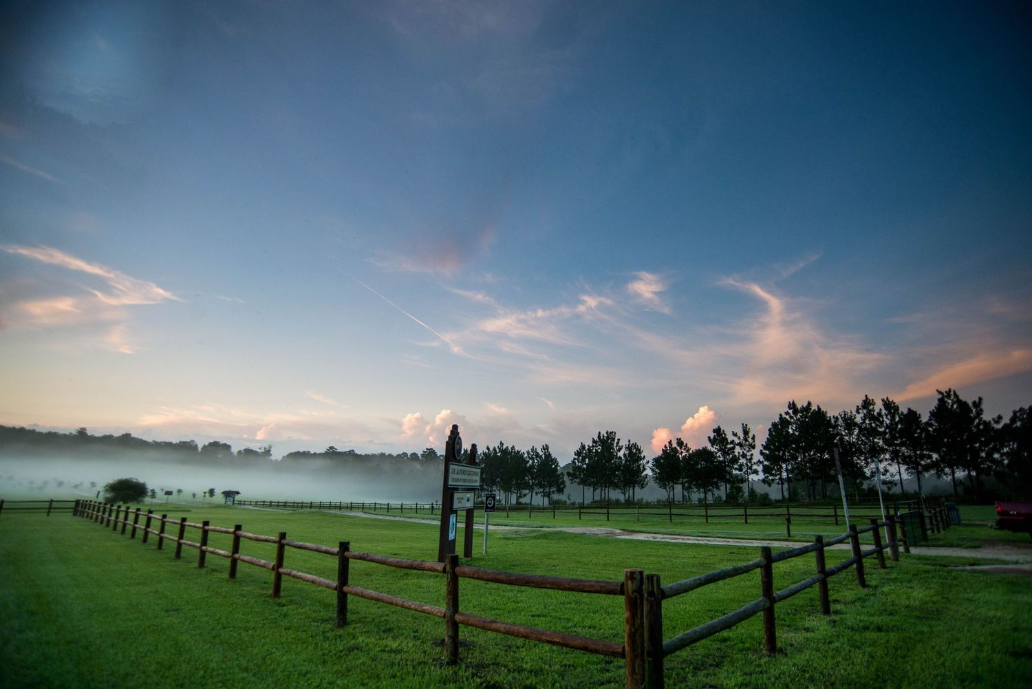 Panoramic view of a green pasture with wooden fence posts stretching into the distance under a dramatic sunset sky.