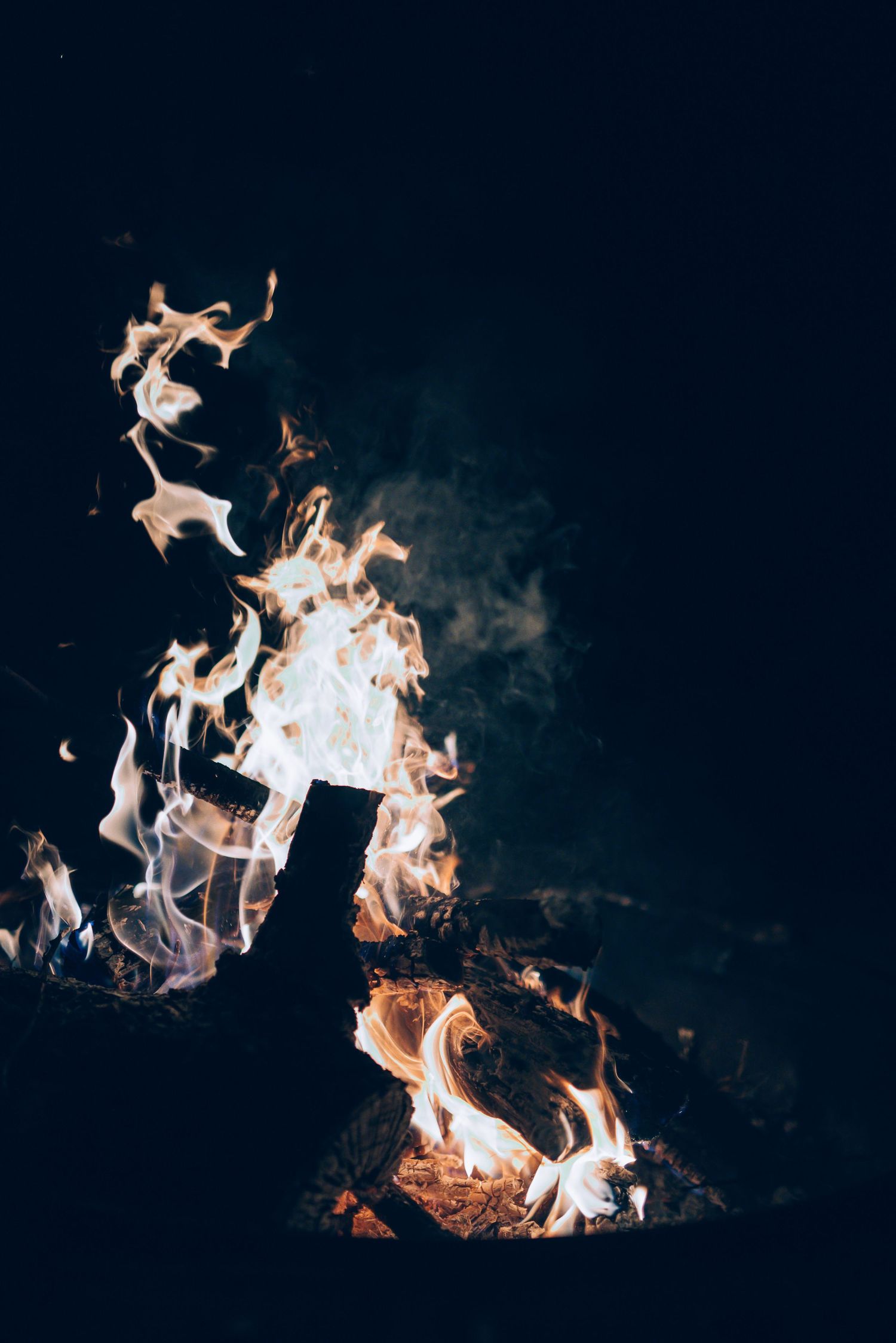 Bright orange flames dancing in darkness with swirling smoke patterns against a black background.
