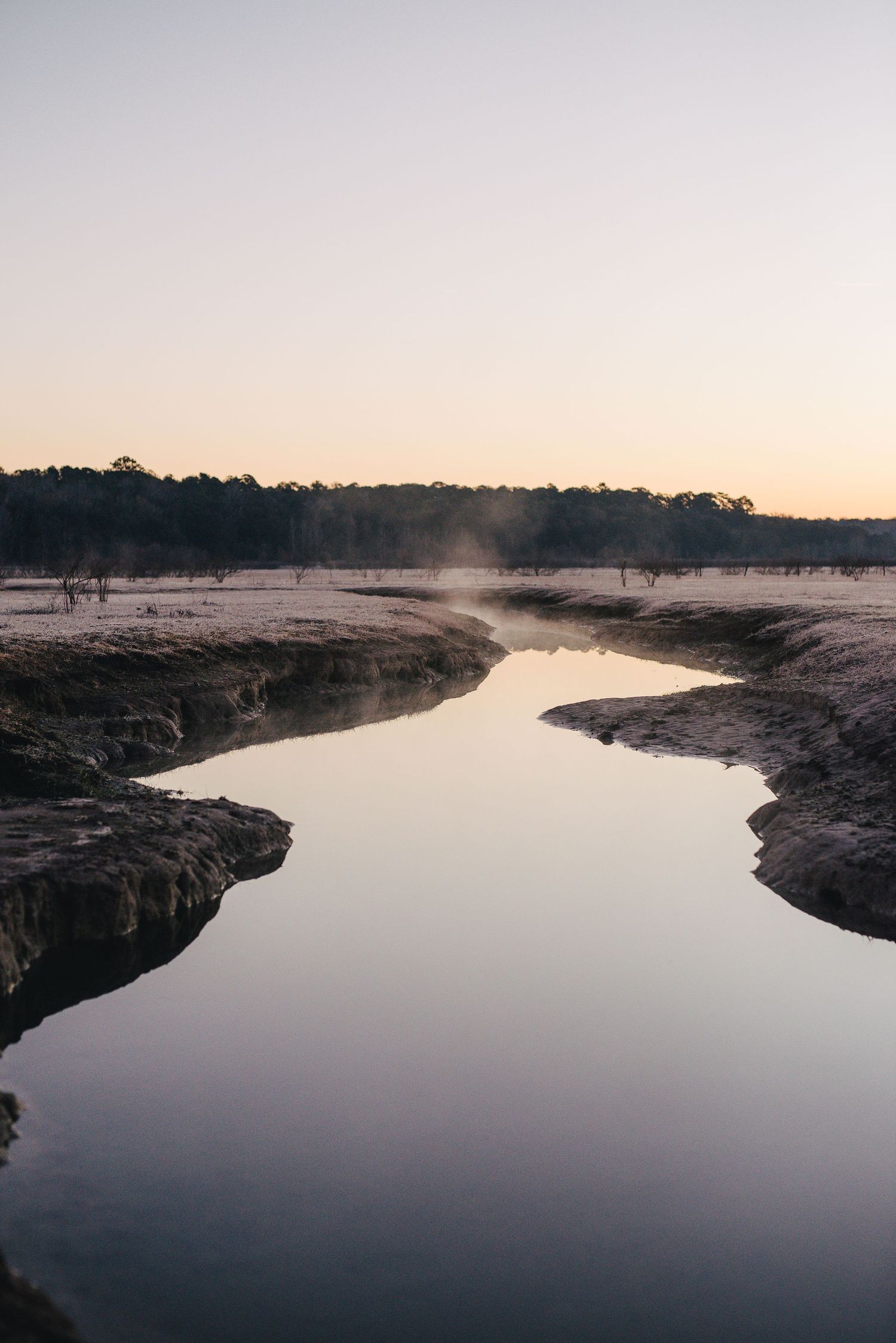 Tranquil river landscape at sunset with misty reflections on calm water and rocky shoreline.