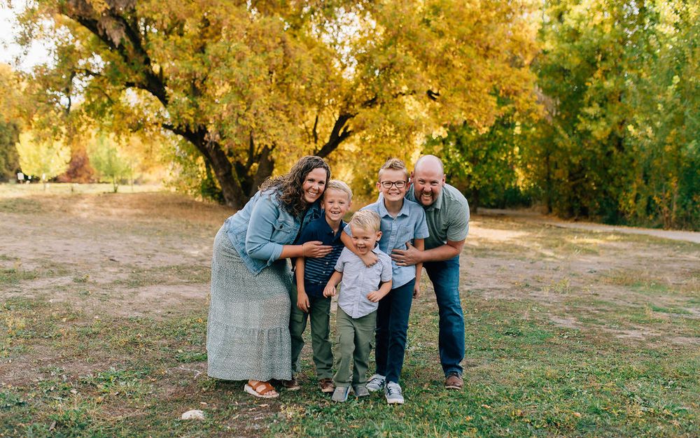 A family sits together on grass during golden hour in a park with autumn trees in the background.
