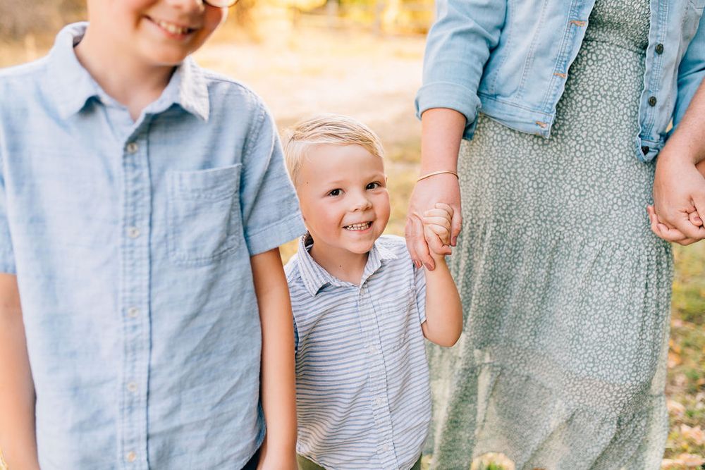 A family group wearing coordinated blue and white outfits poses together outdoors in warm sunlight.