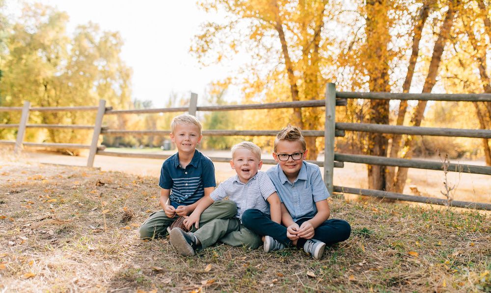 Family members sit together on grass near wooden fence during golden autumn sunset.