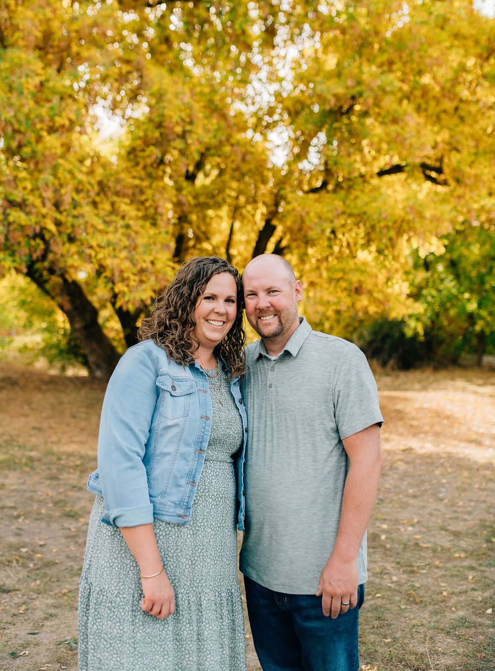 A couple shares an intimate moment together in a park with golden autumn trees in the background.