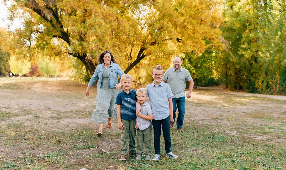 A group in coordinated blue and white outfits poses together in a sun-drenched autumn park with golden foliage.