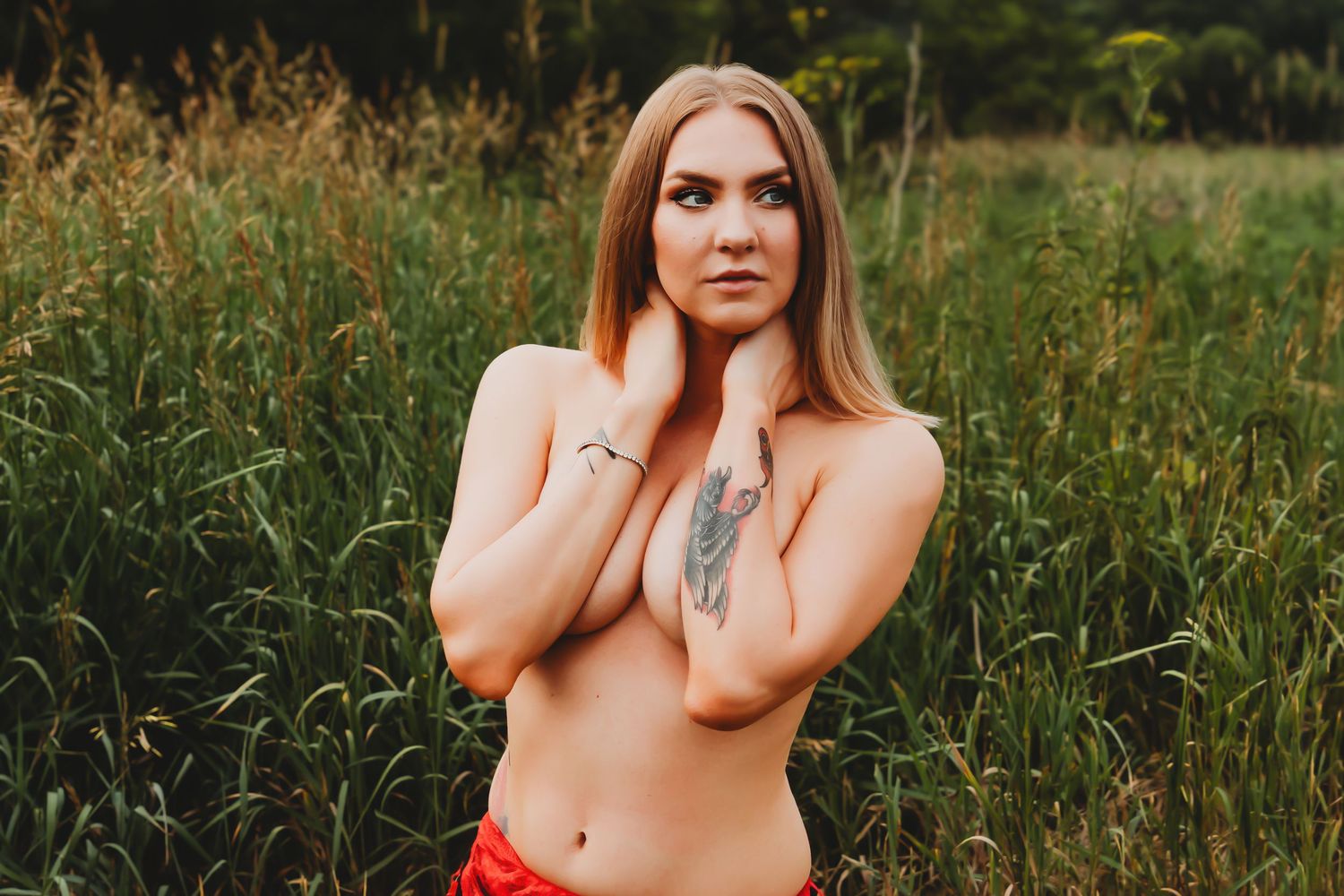 A person poses in a grassy field at golden hour wearing a red top.