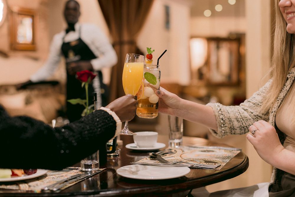 Two people toasting with tropical cocktails at a fine dining restaurant table.