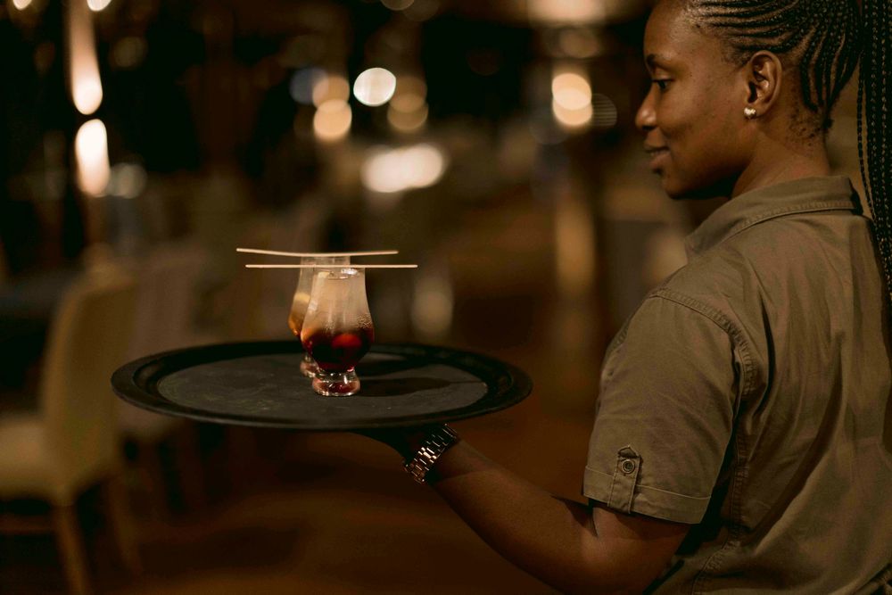 Smiling waitress carrying a tray with a cocktail garnished with chopsticks in a restaurant.