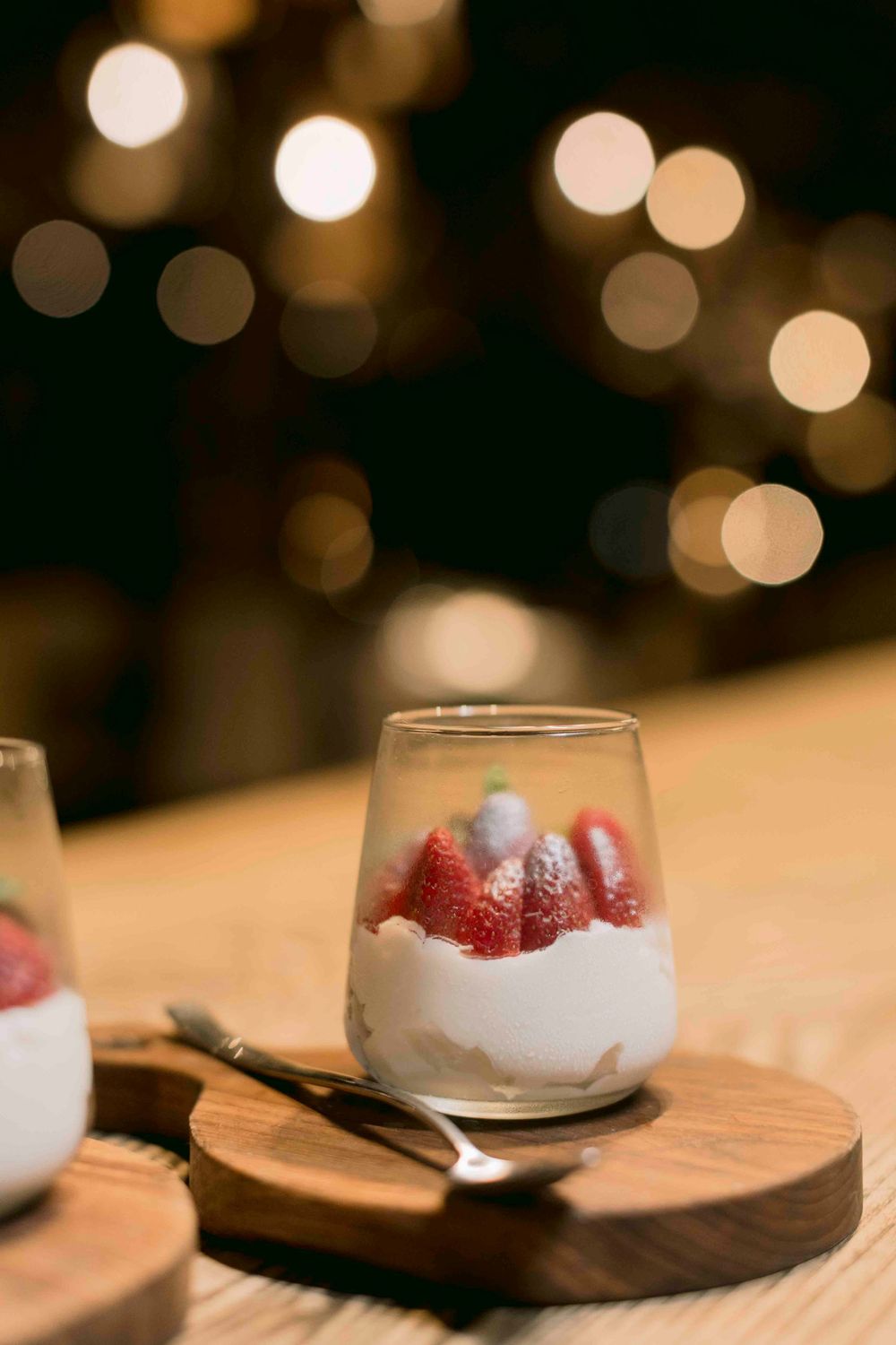 Elegant strawberry and cream dessert in a glass on a wooden board with bokeh lights.