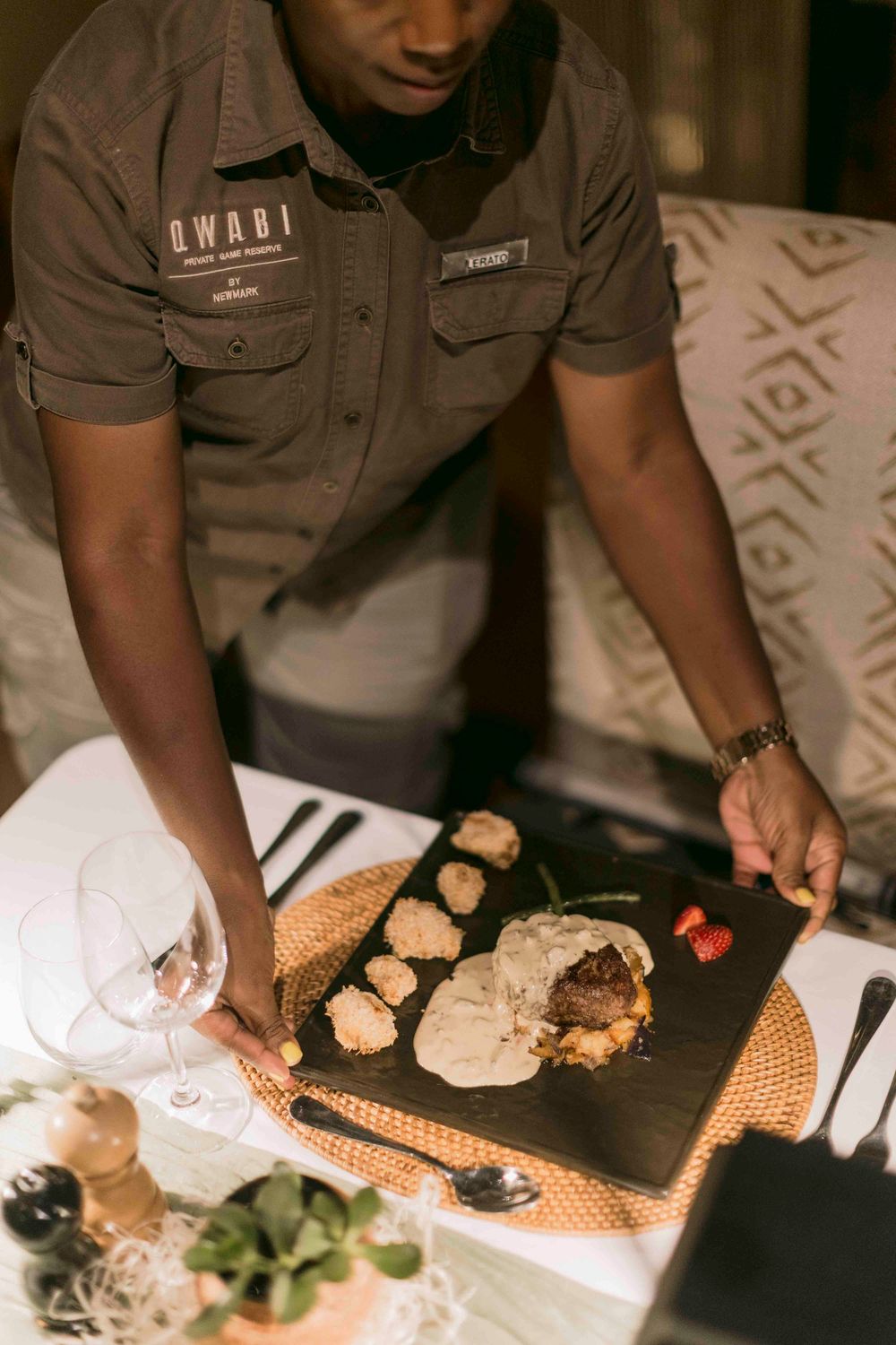 Qwabi restaurant server presenting an elegant steak dish on a slate board at a beautifully set table.
